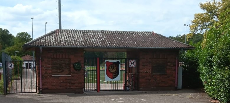 Eingangsbereich einer Sportanlage mit einem kleinen Backsteingebäude und zwei verschlossenen Eingangstoren.