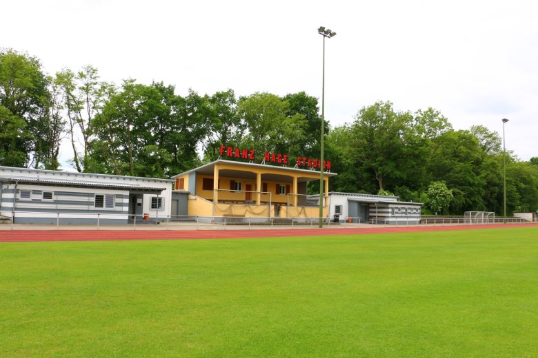 Blick über das Rasenfeld und die rote Laufbahn des Franz-Hage-Stadions auf das zentrale Stadiongebäude und die umliegenden Flutlichtmasten.