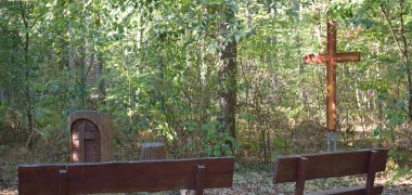 Holzbänke am Andachtsplatz des Waldfriedhofs mit Gedenkstele und großem Holzkreuz im Hintergrund.