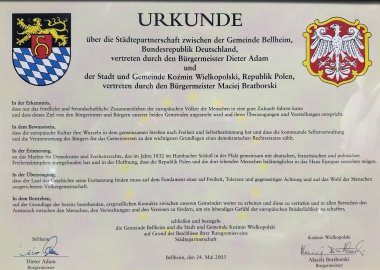 Partnerschaftsurkunde zwischen Bellheim und Koźmin Wielkopolski, unterzeichnet am 24. Mai 2003 von den Bürgermeistern Dieter Adam und Maciej Bratborski inklusive Darstellung der beiden Wappen.
