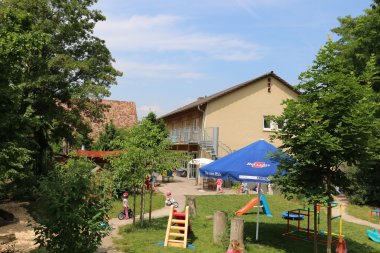 Außengelände der Kindertagesstätte St. Georg in Knittelsheim mit Bäumen, Rutsche und weiteren Spielgeräten sowie spielenden Kindern vor dem Gebäude.
