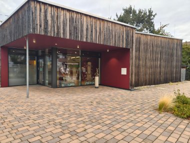 Außenansicht der Kindertagesstätte „Hasenspiel“ mit moderner Holzfassade, dunkelrotem Eingangsbereich und großen, kindgerecht dekorierten Fensterflächen.